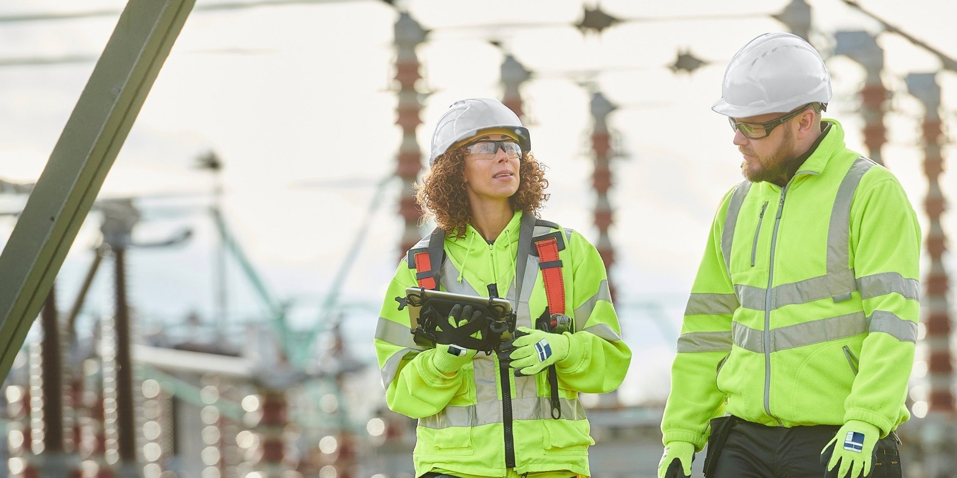 Engineer in a white hard hat and hi-vis holding a tablet at a substation
