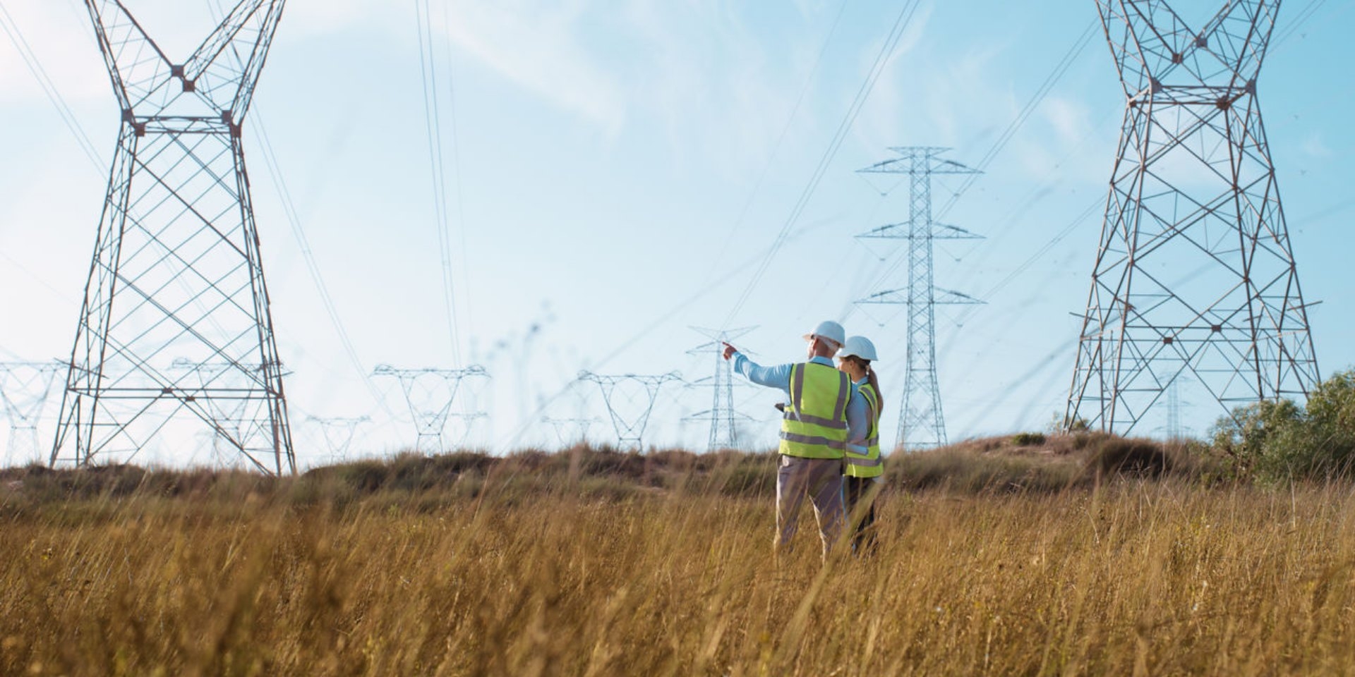 Two engineers in hi-vis surveying a field beneath overhead power lines
